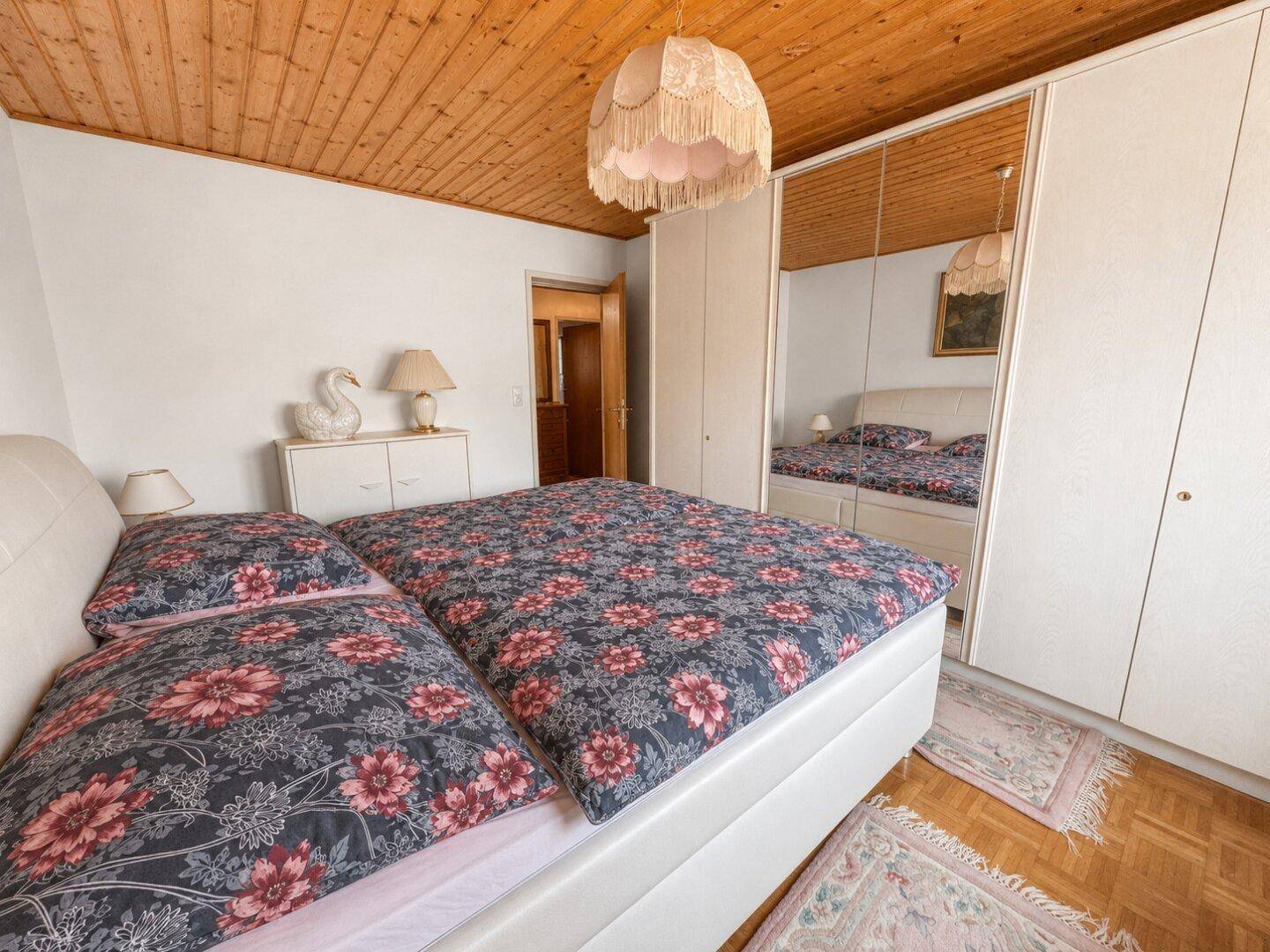 Schlafzimmer mit Doppelbett, Spiegelschrank und Holzparkettboden, gemütliche Atmosphäre.
