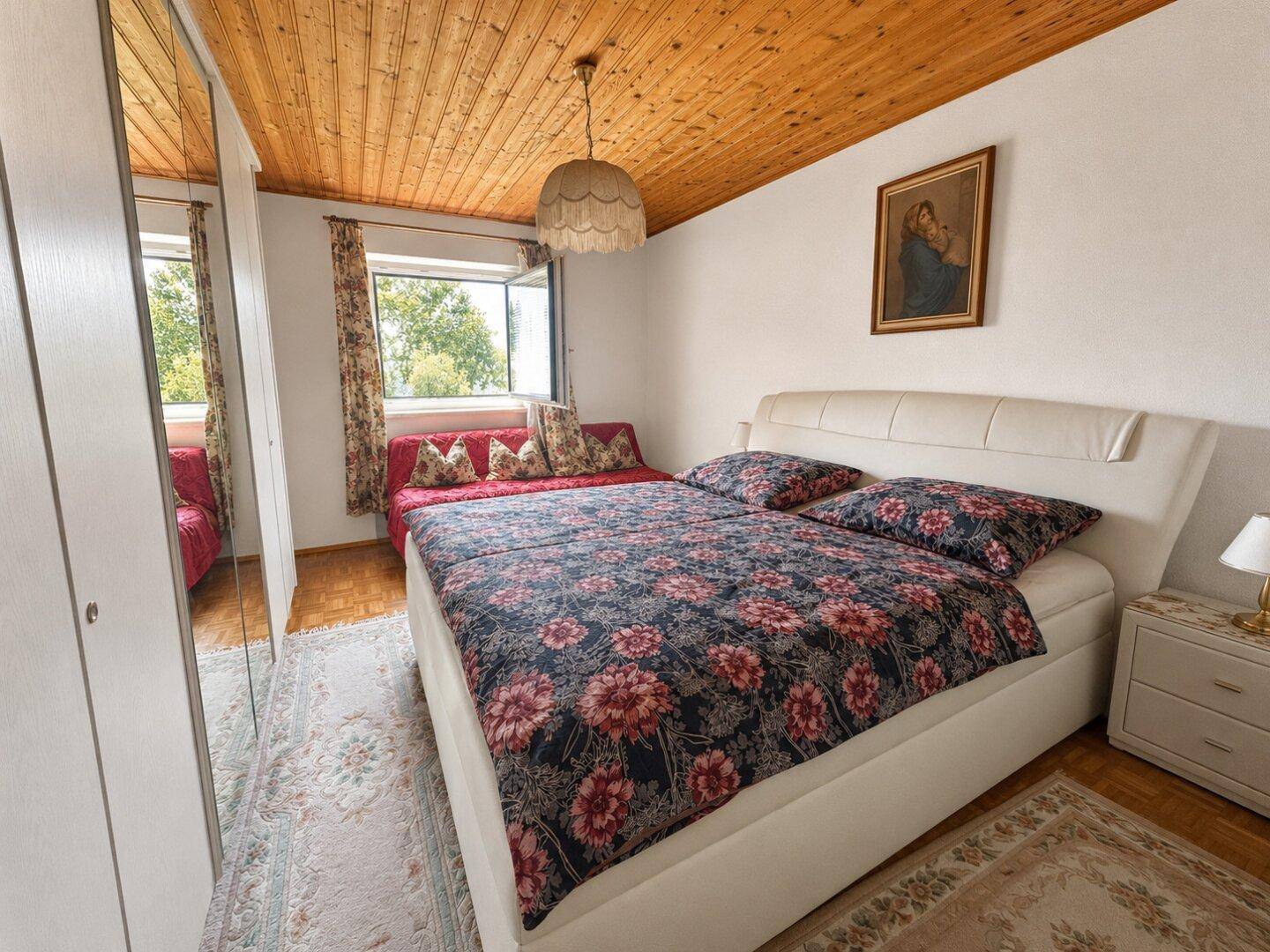 Gemütliches Schlafzimmer mit Holzbalkendecke, Doppelbett und einem zusätzlichen Schlafsofa am Fenster.