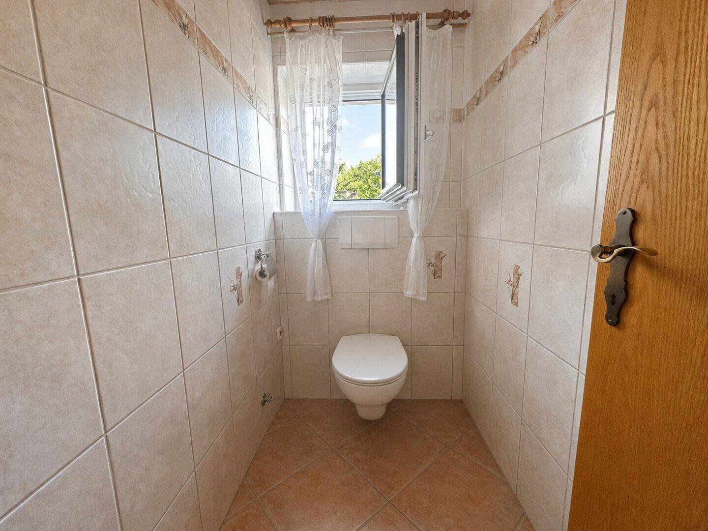 Kleines, hell gefliestes WC mit Fenster für natürliche Belüftung und Tageslicht.