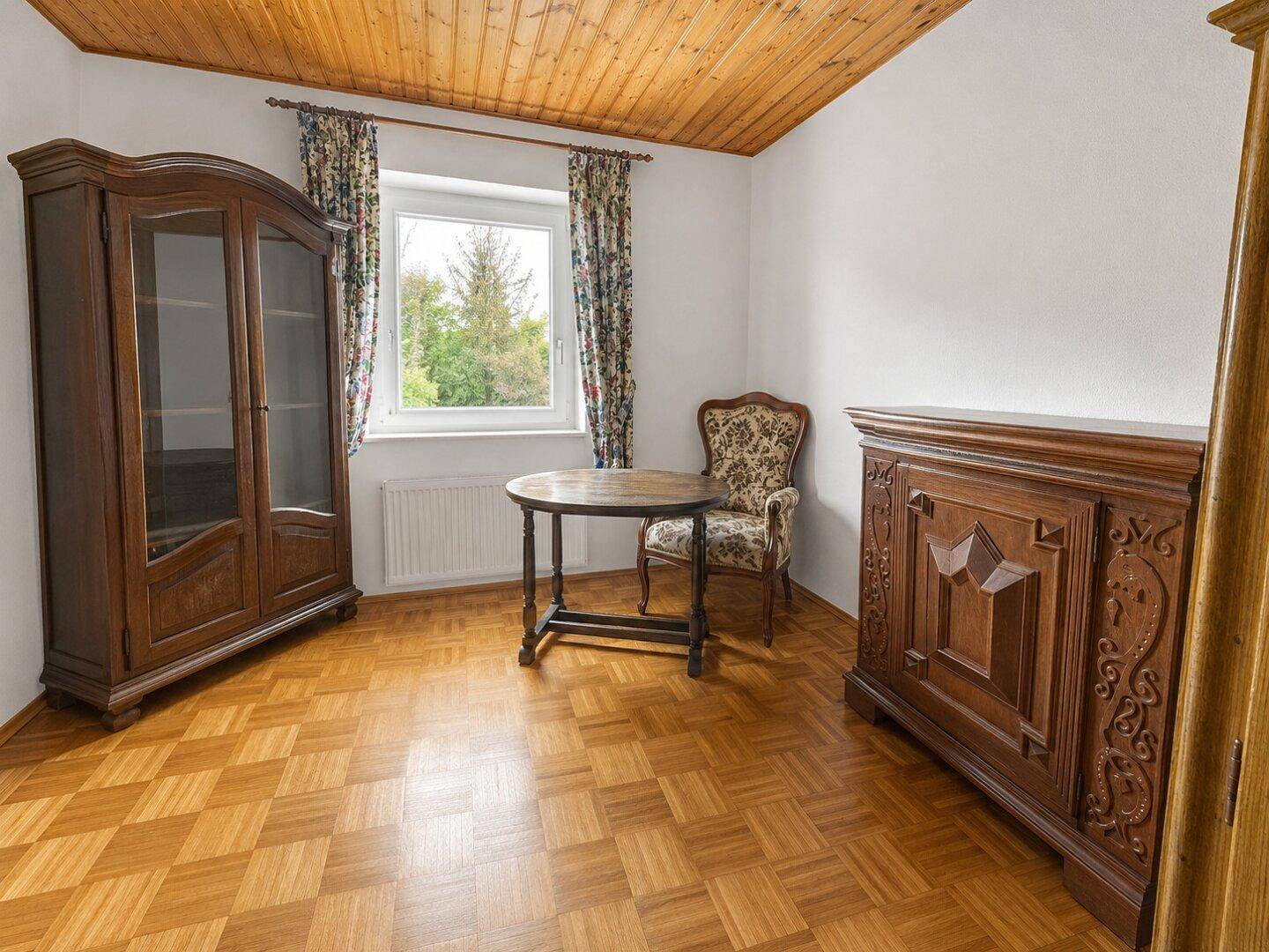 Geräumiges Zimmer mit Parkettboden, traditionellen Holzmöbeln und Blick ins Grüne.