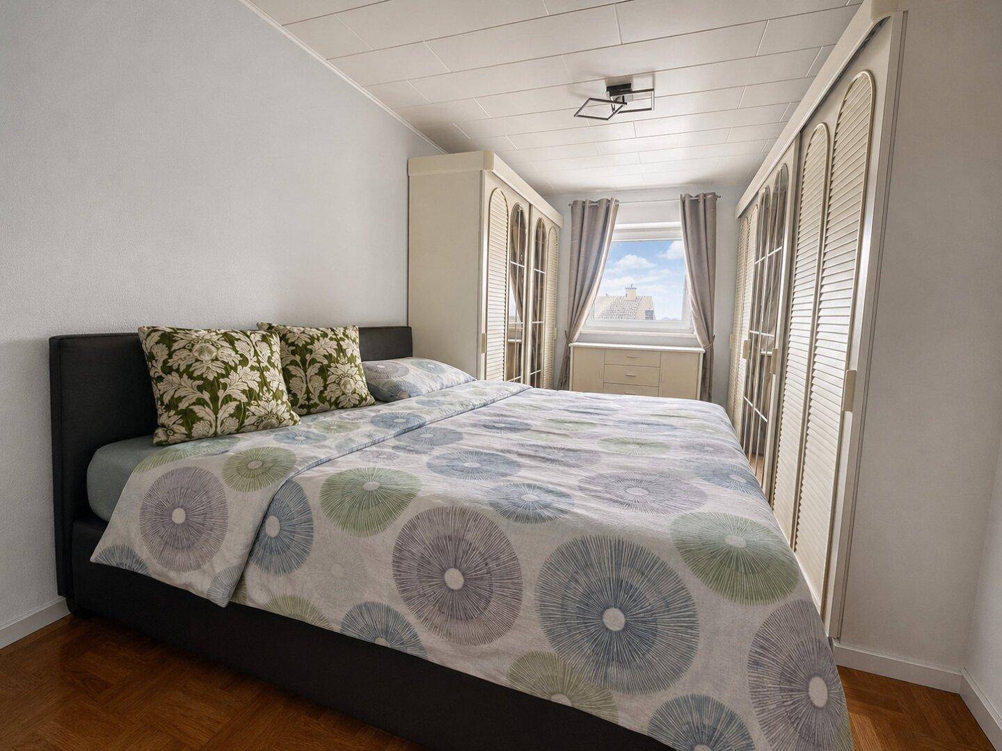 Helles Schlafzimmer mit Doppelbett und Einbauschränken, Blick aus dem Fenster.