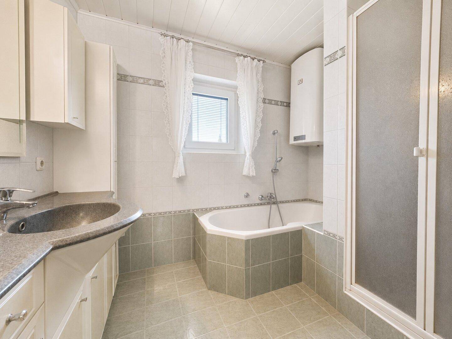 Badezimmer mit Eckbadewanne, Duschkabine und Fenster, hell gefliest.