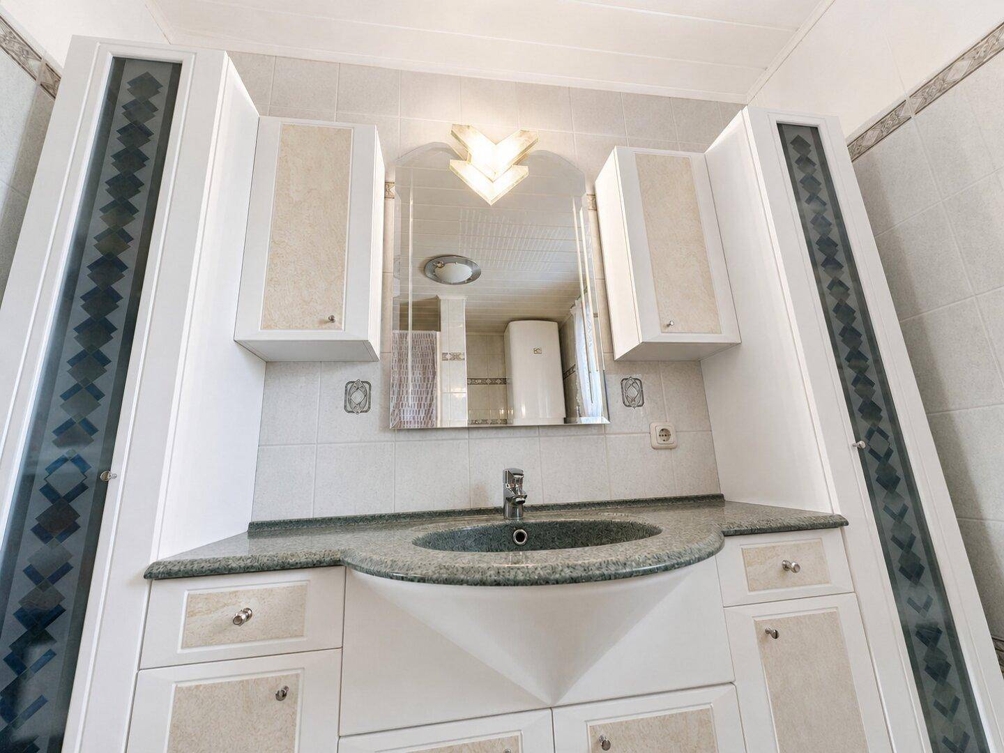 Badezimmermöbel mit Waschbecken, Spiegelschrank und seitlichen Hochschränken.