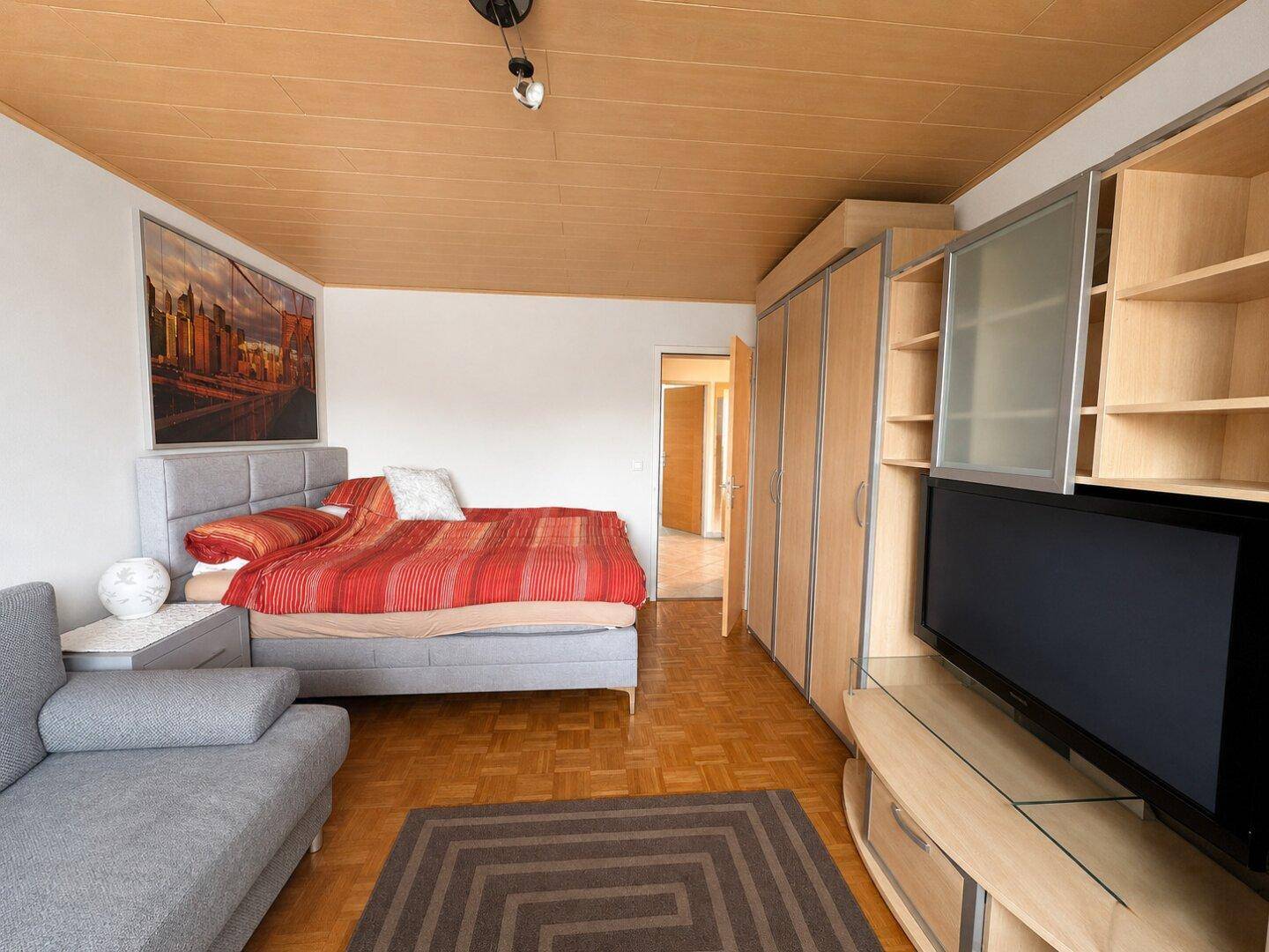 Schlafzimmer mit Bett, Sofa und integriertem Schranksystem mit Fernseher.