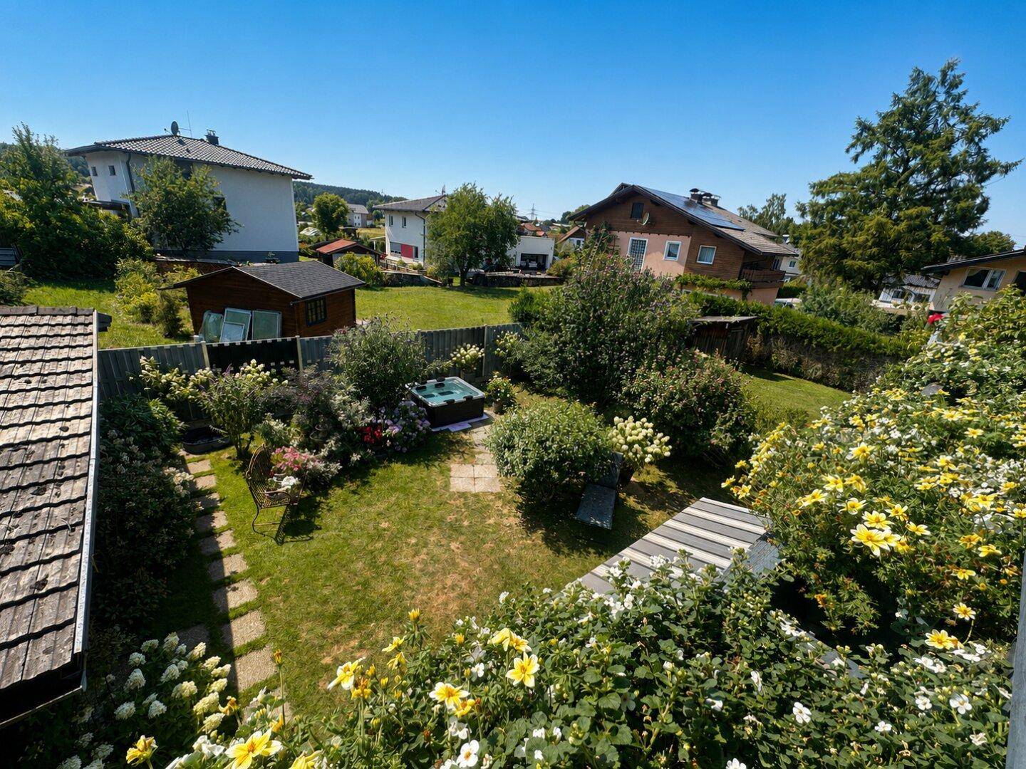 Sonniger Garten mit Whirlpool, umgeben von blühenden Pflanzen und Hecken.