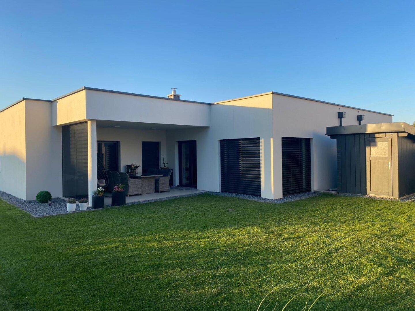 Modernes Einfamilienhaus mit gepflegtem Garten und sonniger Terrasse am Abend.