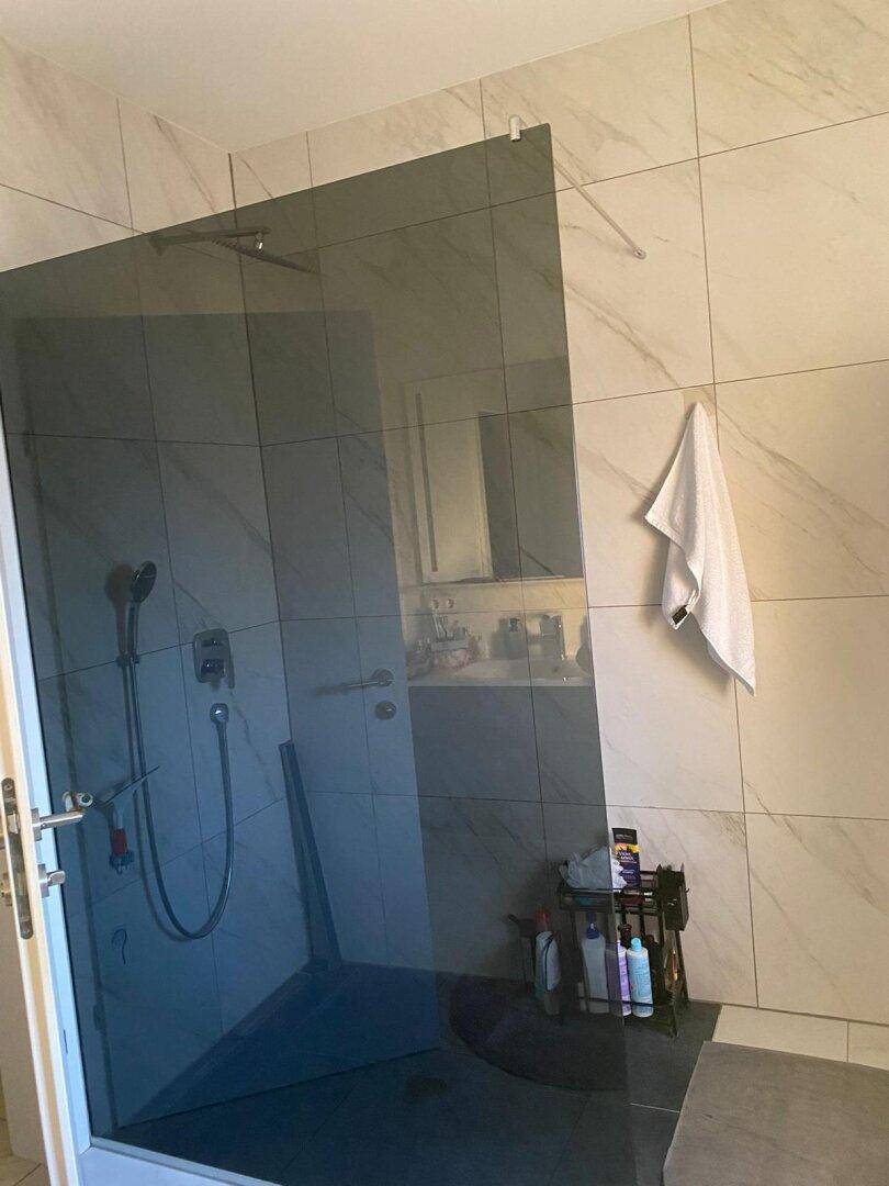 Modernes Badezimmer mit großer begehbarer Dusche und eleganten großformatigen Fliesen.