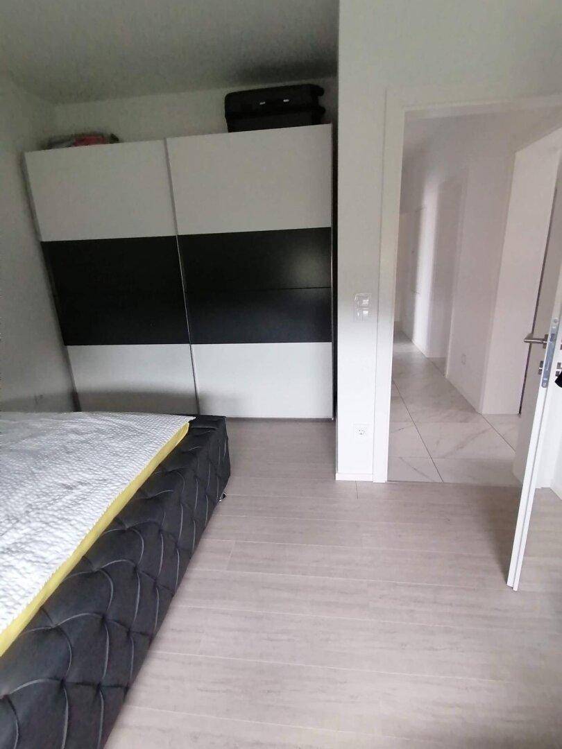 Schlafzimmer mit modernem Bett, großem Schiebetürenschrank und hellem Laminatboden.