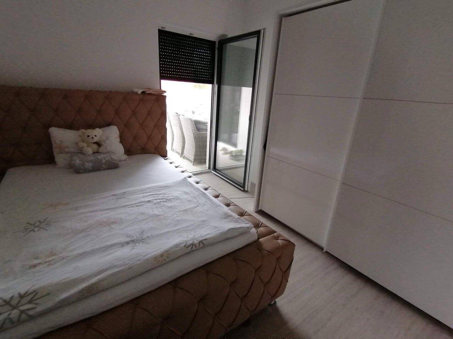 Schlafzimmer mit Bett und direktem Zugang zu einem Außenbereich durch eine Glastür mit Rollladen.
