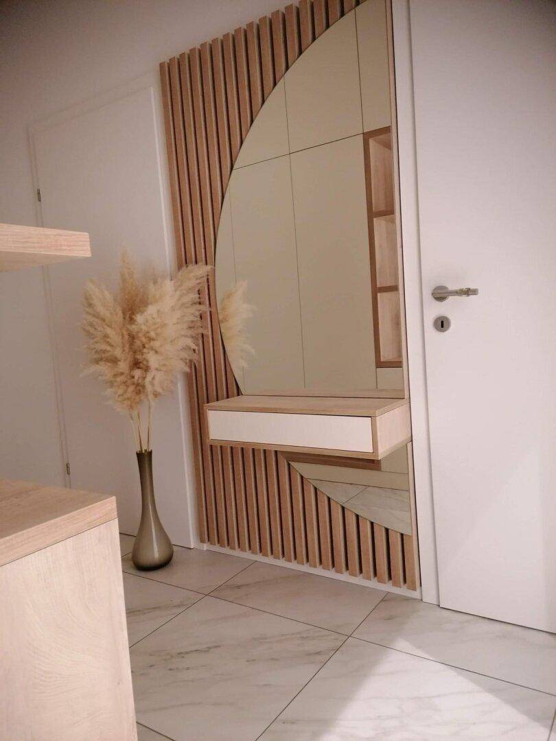 Detailansicht des Eingangsbereichs mit modernem Spiegel, Holzlamellen und Fliesenboden.