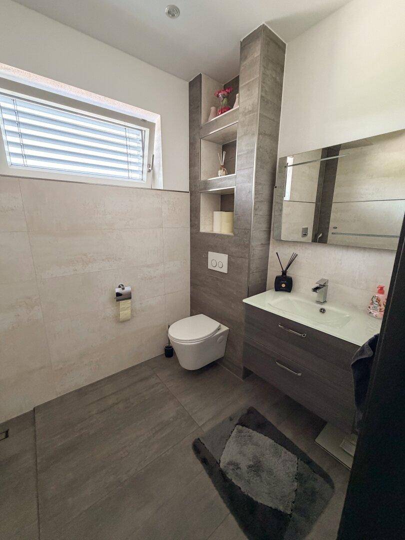 Modernes Gäste-WC mit wandhängendem WC, Einzelwaschbecken und Fenster für Tageslicht.