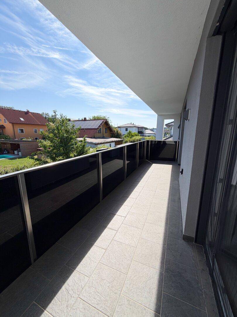 Langer, moderner Balkon mit Fliesenboden und Glasgeländer, bietet Ausblick auf die Umgebung.