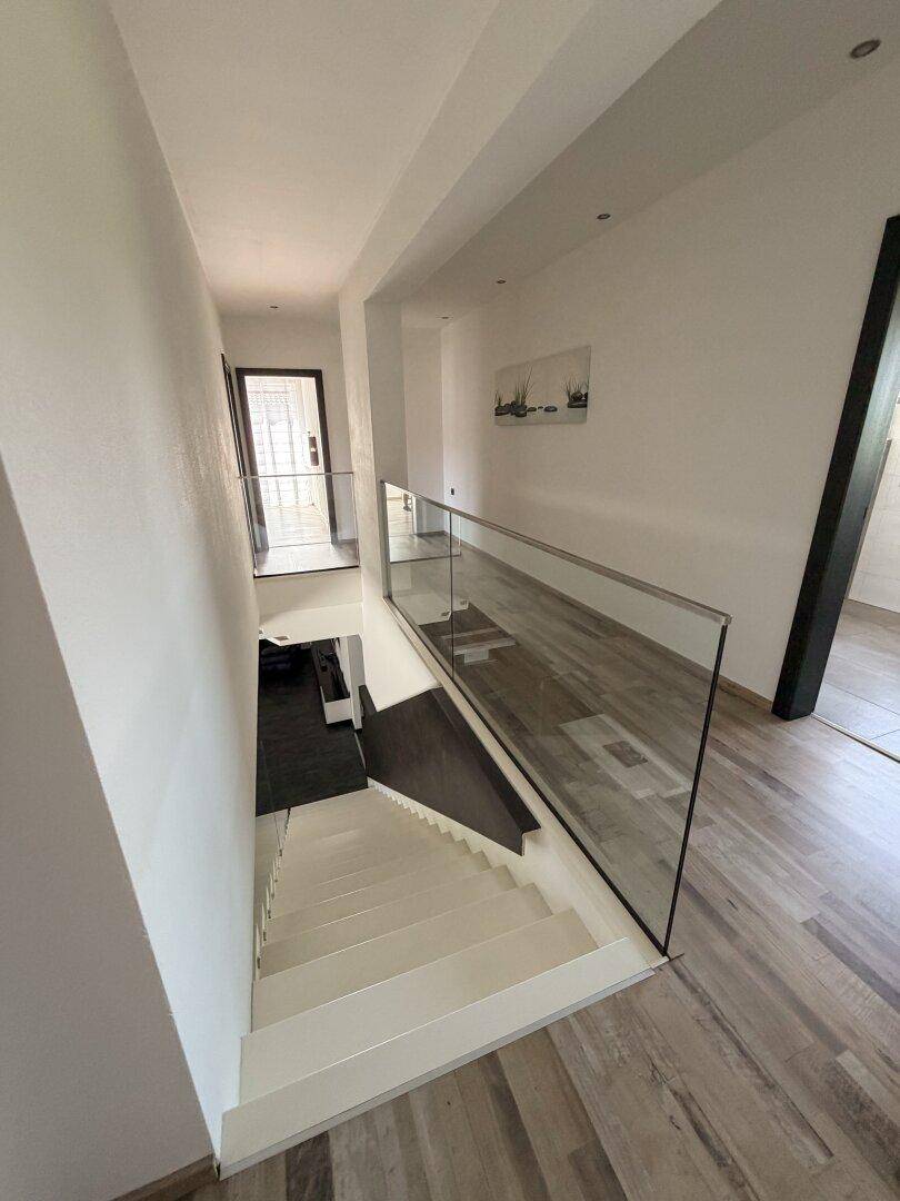 Heller Flur im Obergeschoss mit Blick auf die Treppe und modernem Glasgeländer.