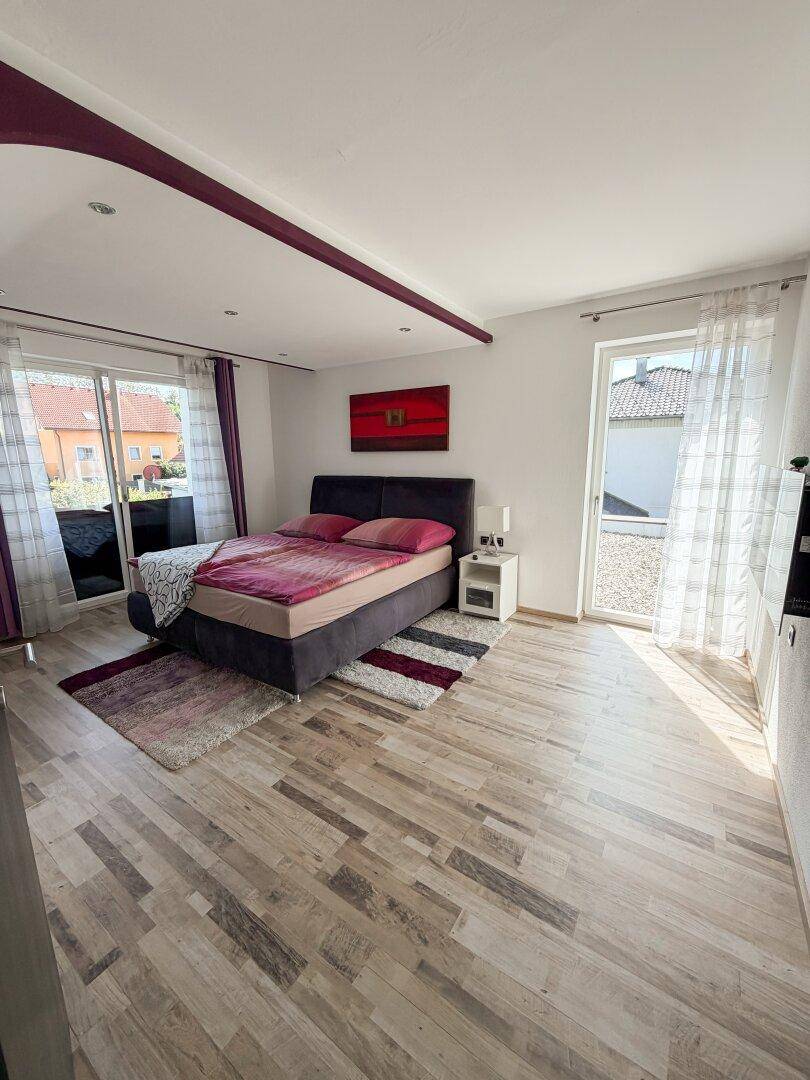 Helles Schlafzimmer mit Doppelbett, Nachttischen und Zugang zu einem Außenbereich.