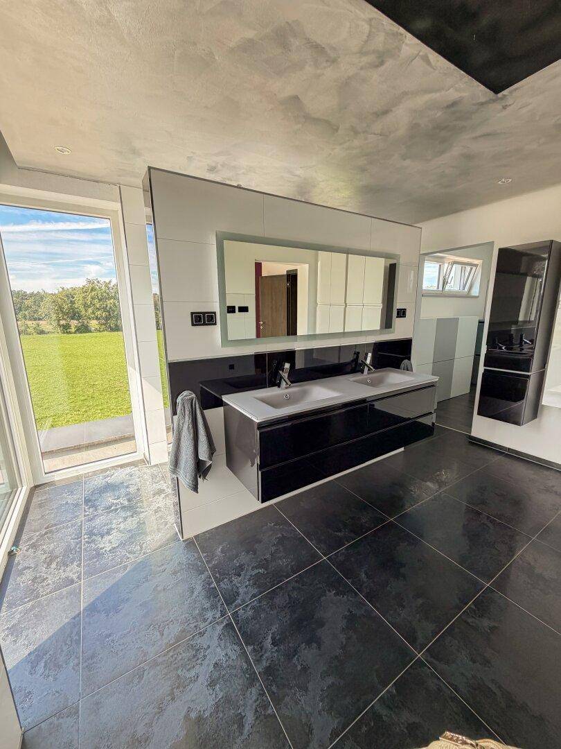 Modernes Badezimmer mit Doppelwaschbecken, großem Spiegel und weitem Blick ins Grüne.