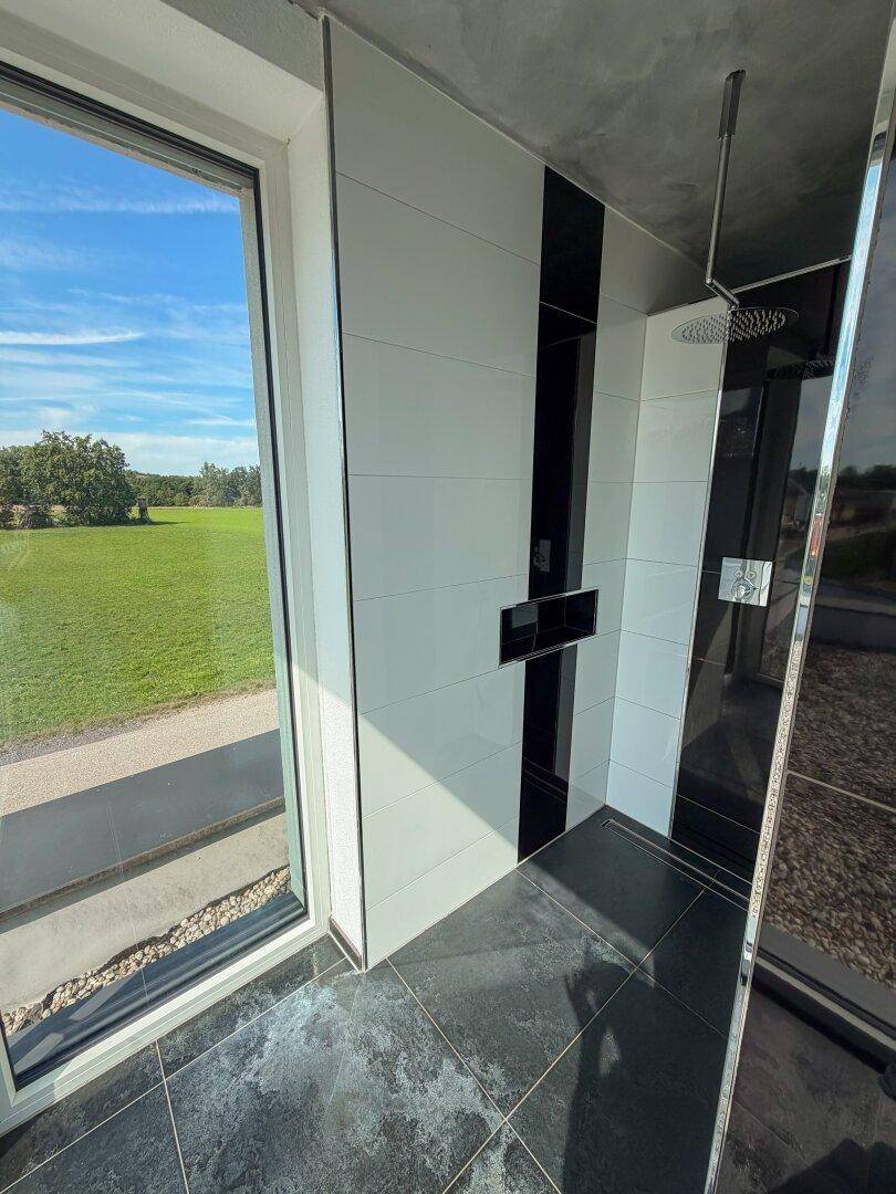 Geräumige begehbare Dusche mit Regenduschkopf und großem Fenster mit Blick ins Grüne.