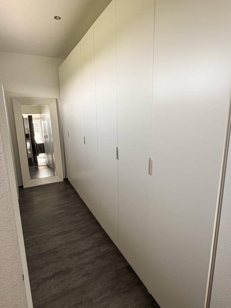 Heller Flur mit integrierten weißen Kleiderschränken und einem großen Wandspiegel.