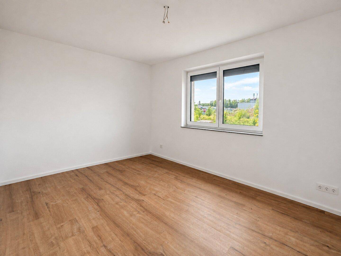 Freundliches Schlafzimmer mit Laminatboden und Ausblick auf grüne Bäume.