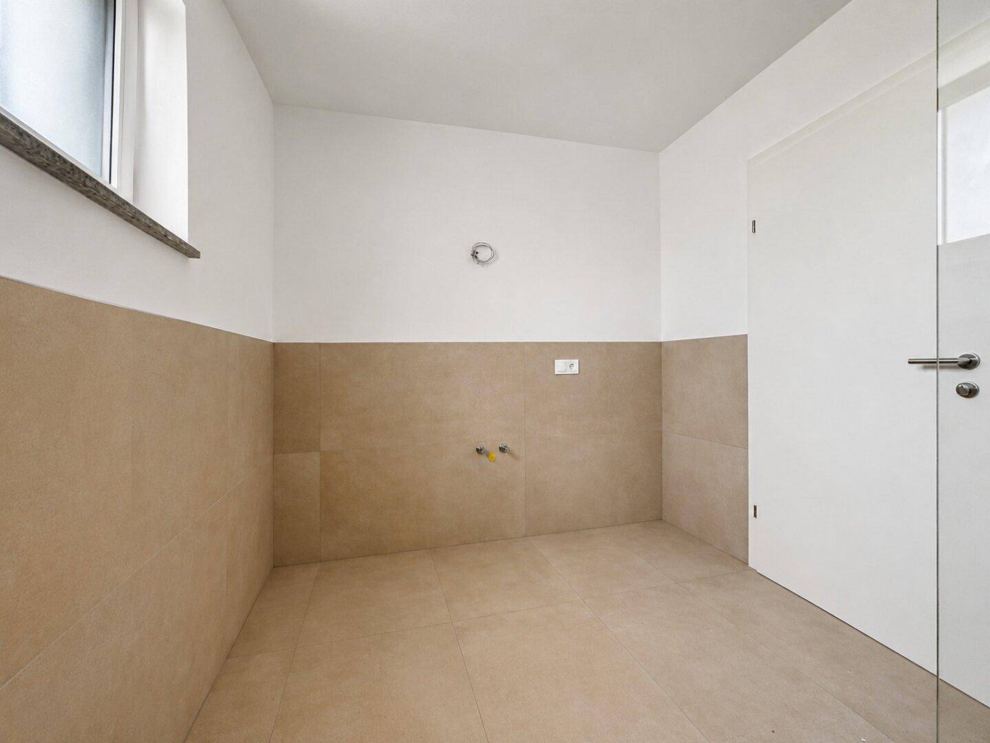 Funktionaler Raum mit beigefarbenen Fliesen und Anschlüssen für Sanitärinstallationen.
