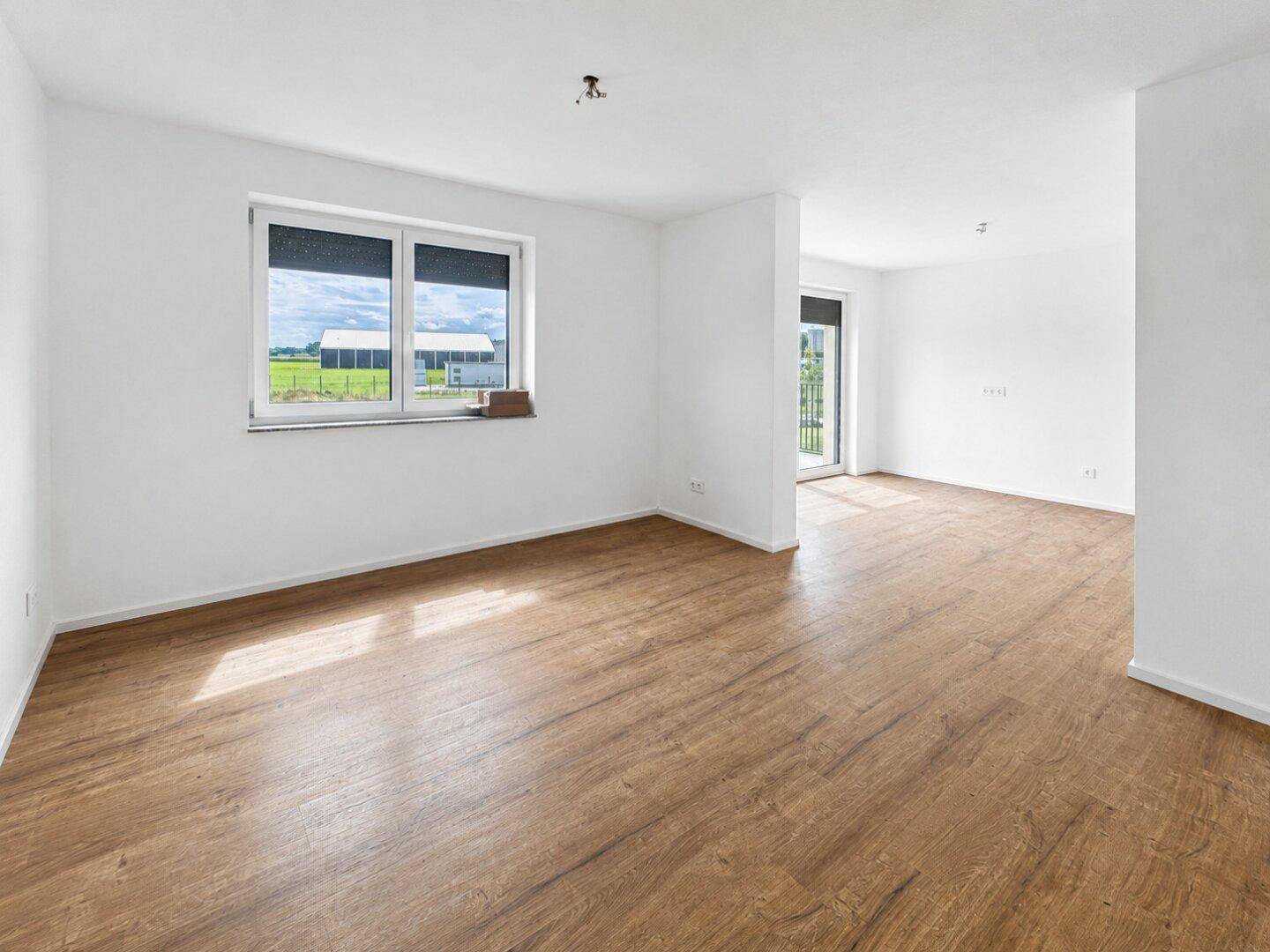 Heller, leerer Raum mit modernem Laminatboden und Blick ins Grüne.