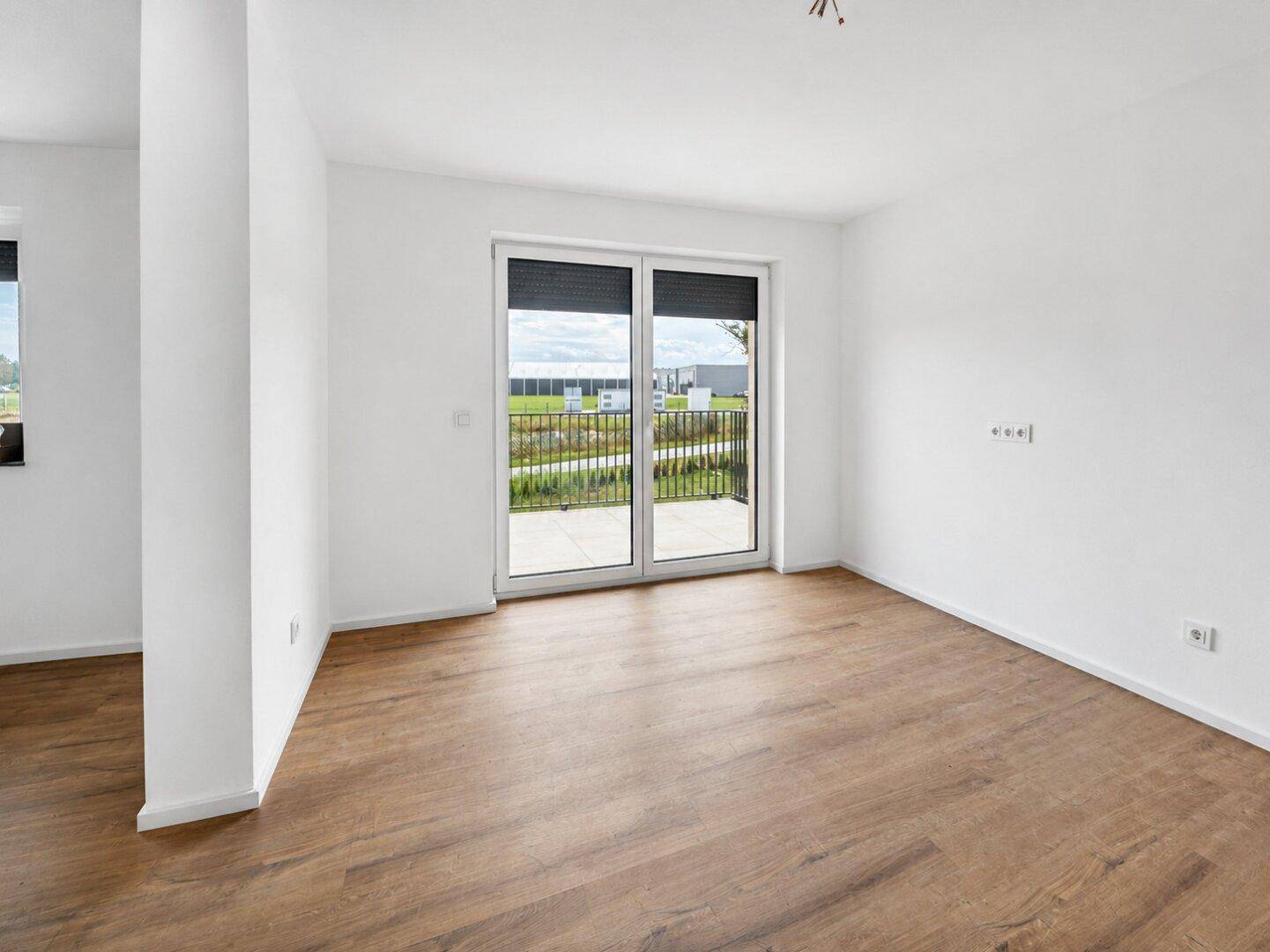 Lichtdurchfluteter Raum mit Laminatboden und Zugang zu einem französischen Balkon.