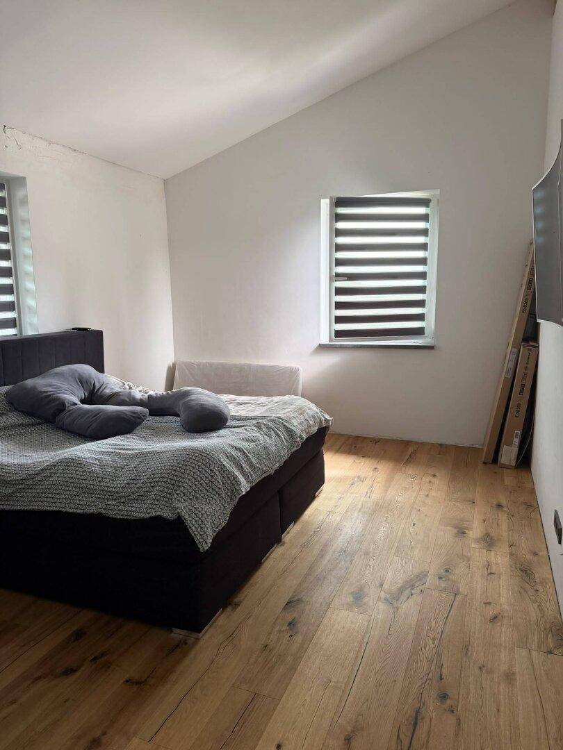 Schlafzimmer mit Holzdielenboden, großem Bett und schräger Decke unter dem Dach.