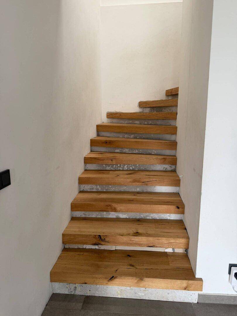 Holztreppe mit sichtbaren Betonstufen, die in die oberen Stockwerke führt.