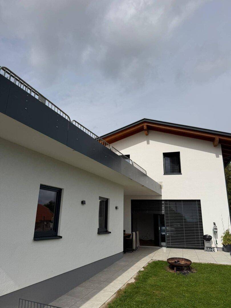 Ansicht des modernen Hauses mit großer Terrasse im Obergeschoss und gepflegtem Rasenbereich.