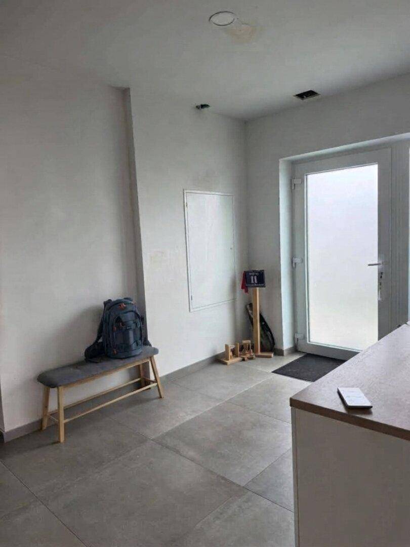 Heller Eingangsbereich mit grauen Fliesen, einer Sitzbank und einer modernen Glastür.
