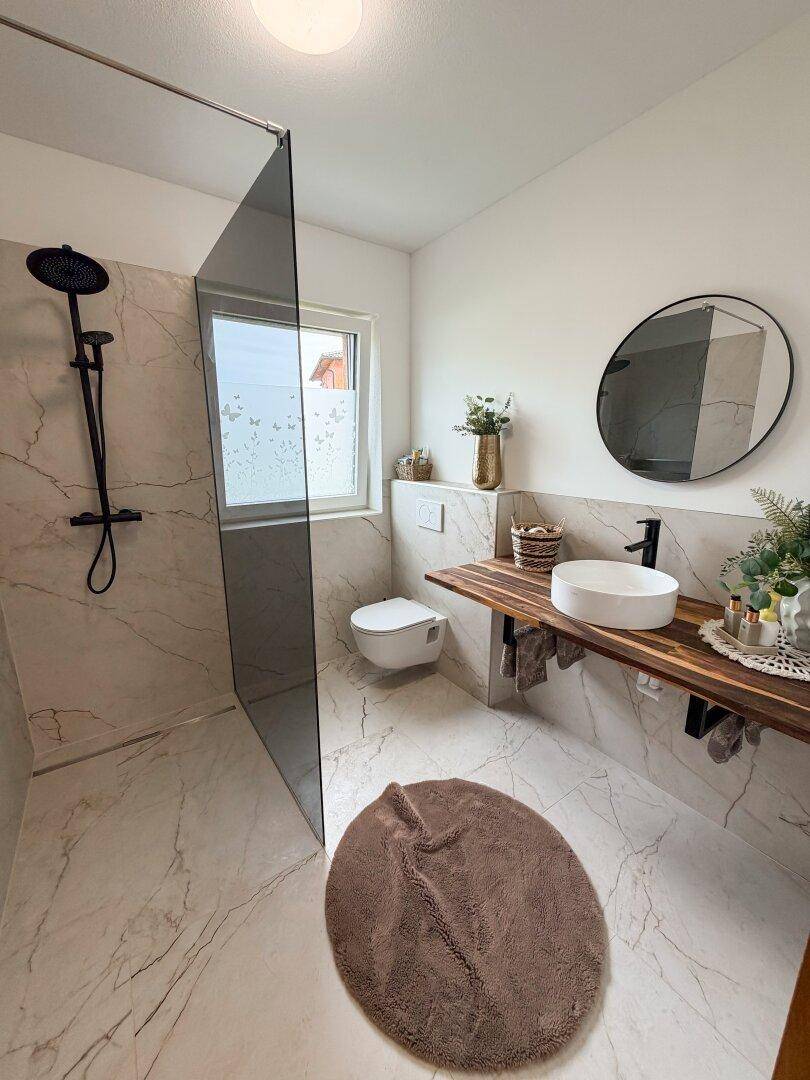 Modernes Badezimmer mit begehbarer Dusche, wandhängendem WC und Einzelwaschbecken auf Holzplatte.