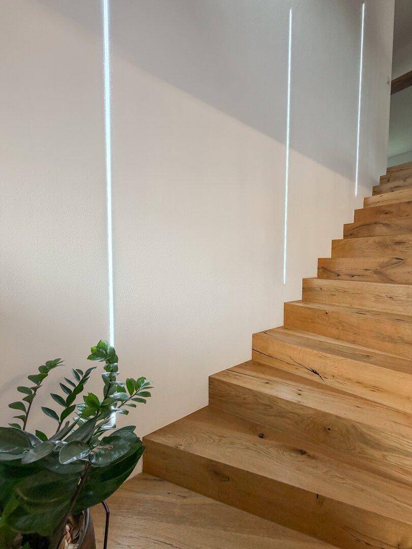 Elegante Holztreppe mit integrierter vertikaler Beleuchtung an der Wand.