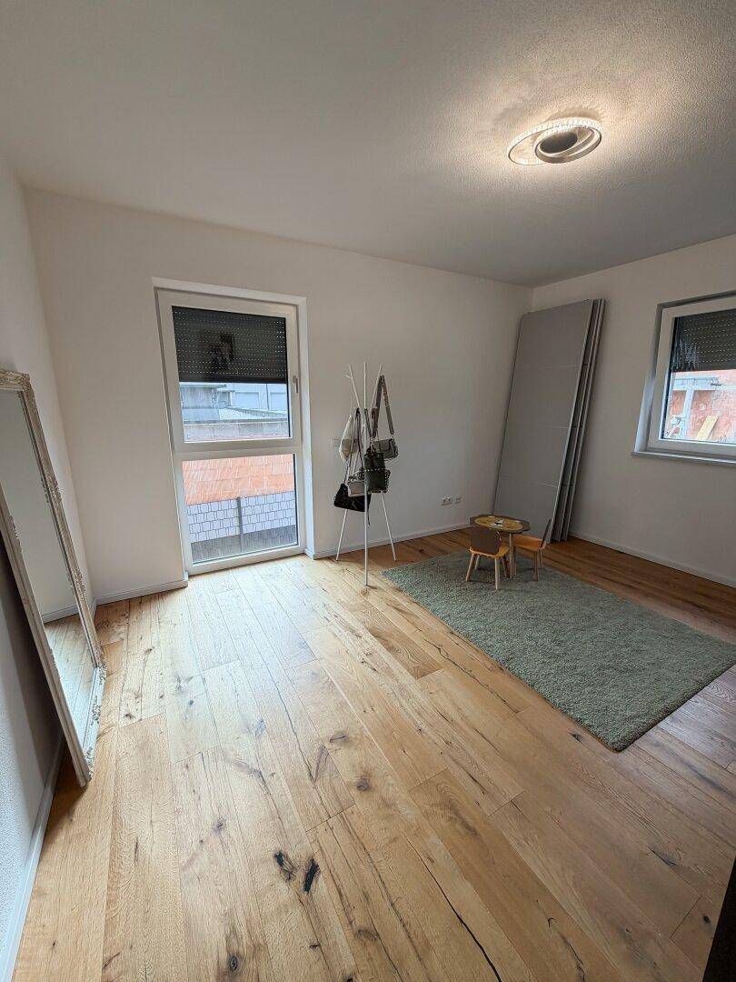 Helles Zimmer mit Holzboden, großem Fenster und Zugang zu einem französischen Balkon.