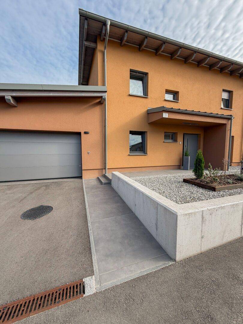Modernes Haus mit orangefarbener Fassade, Garage und barrierefreier Rampe zum Eingang.