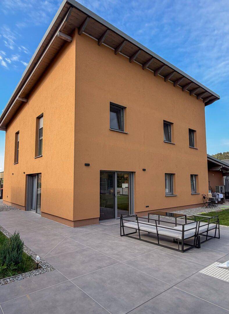Rückseite des Hauses mit orangefarbener Fassade, großen Glasfronten und einer gefliesten Terrasse.