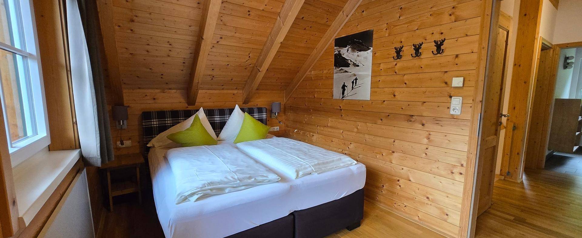 Gemütliches Schlafzimmer im Dachgeschoss mit Holzwänden, schrägen Decken und Doppelbett.