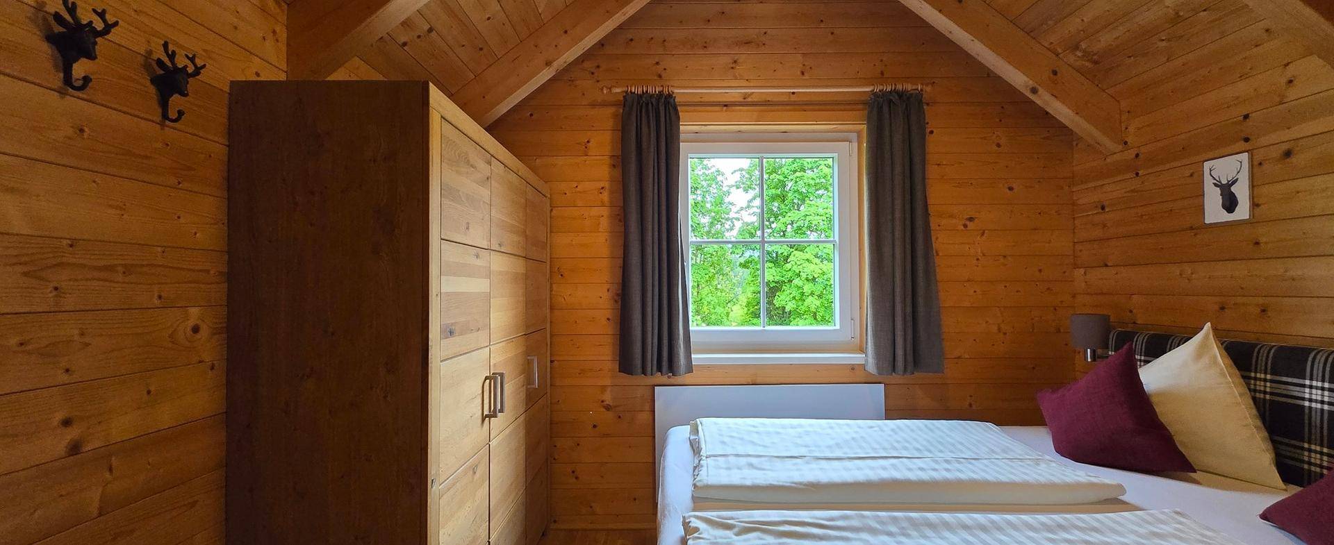Gemütliches Schlafzimmer im Dachgeschoss mit Holzwänden, Fenster und rustikaler Dekoration.