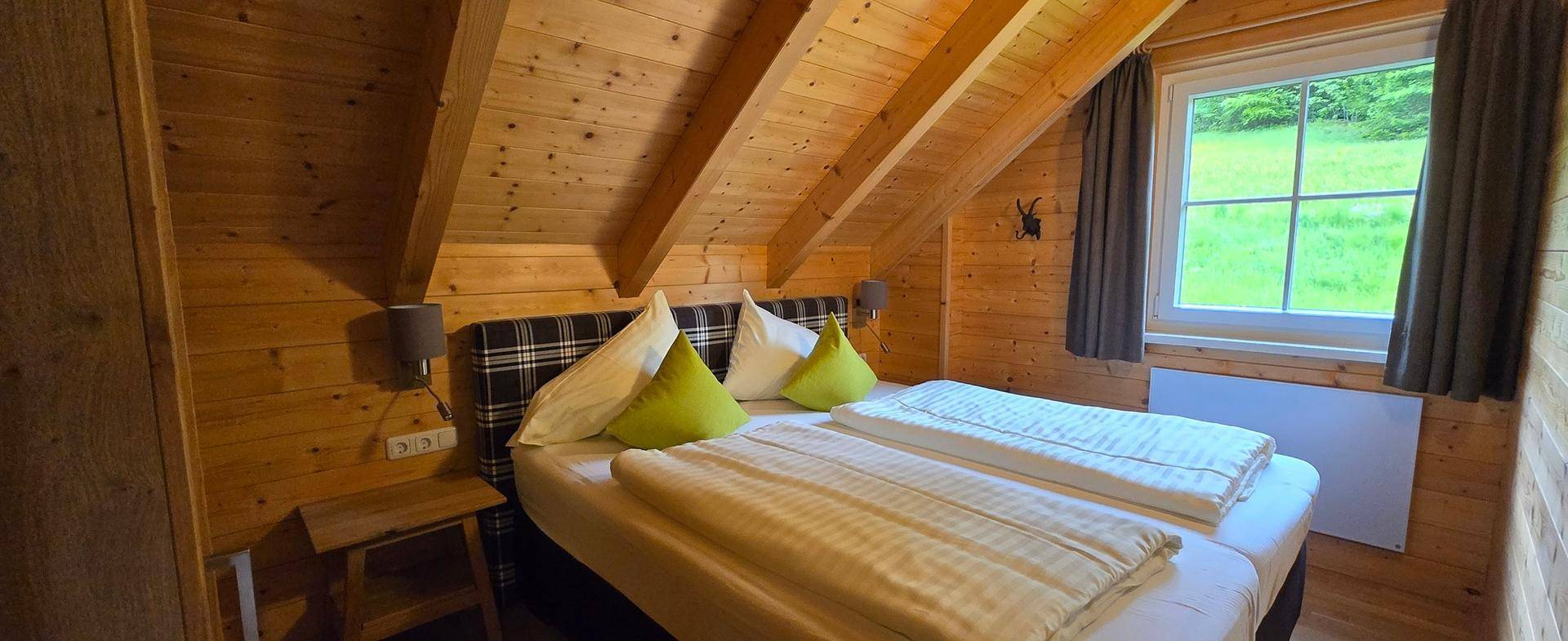 Helles Schlafzimmer im Dachgeschoss mit Holzwänden, Doppelbett und Blick ins Grüne.