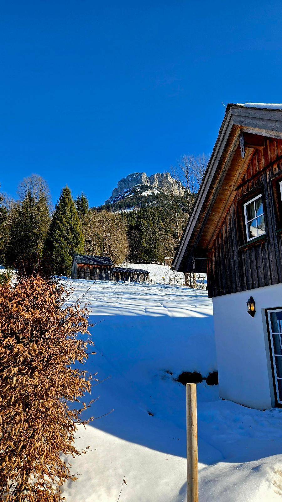 Holzhaus im Winter mit verschneiter Umgebung und majestätischem Bergblick.