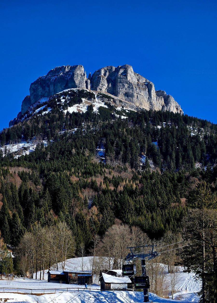 Majestätischer Berg mit verschneiten Hängen und einem Skilift unter strahlend blauem Himmel.