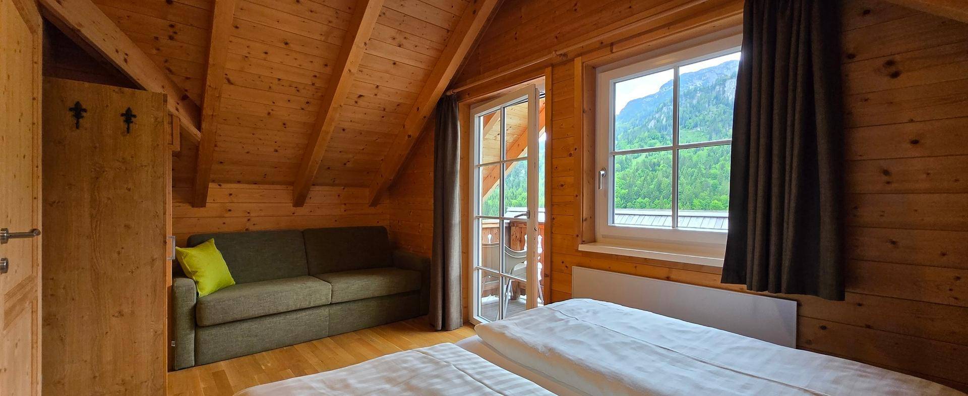 Helles Schlafzimmer im Dachgeschoss mit Holzwänden, Sofa und Bergblick.