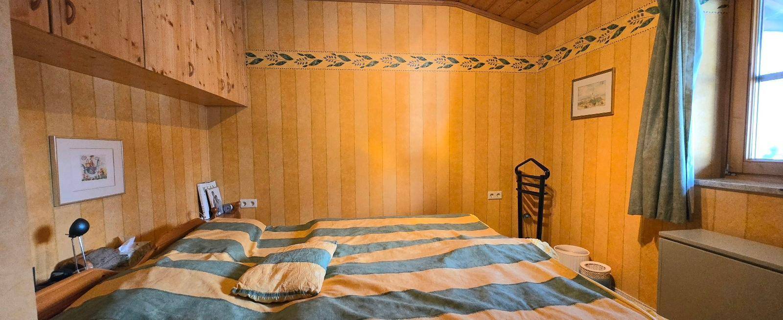 Gemütliches Schlafzimmer mit Holzvertäfelung, gestreifter Bettwäsche und Fenster für natürliches Licht.