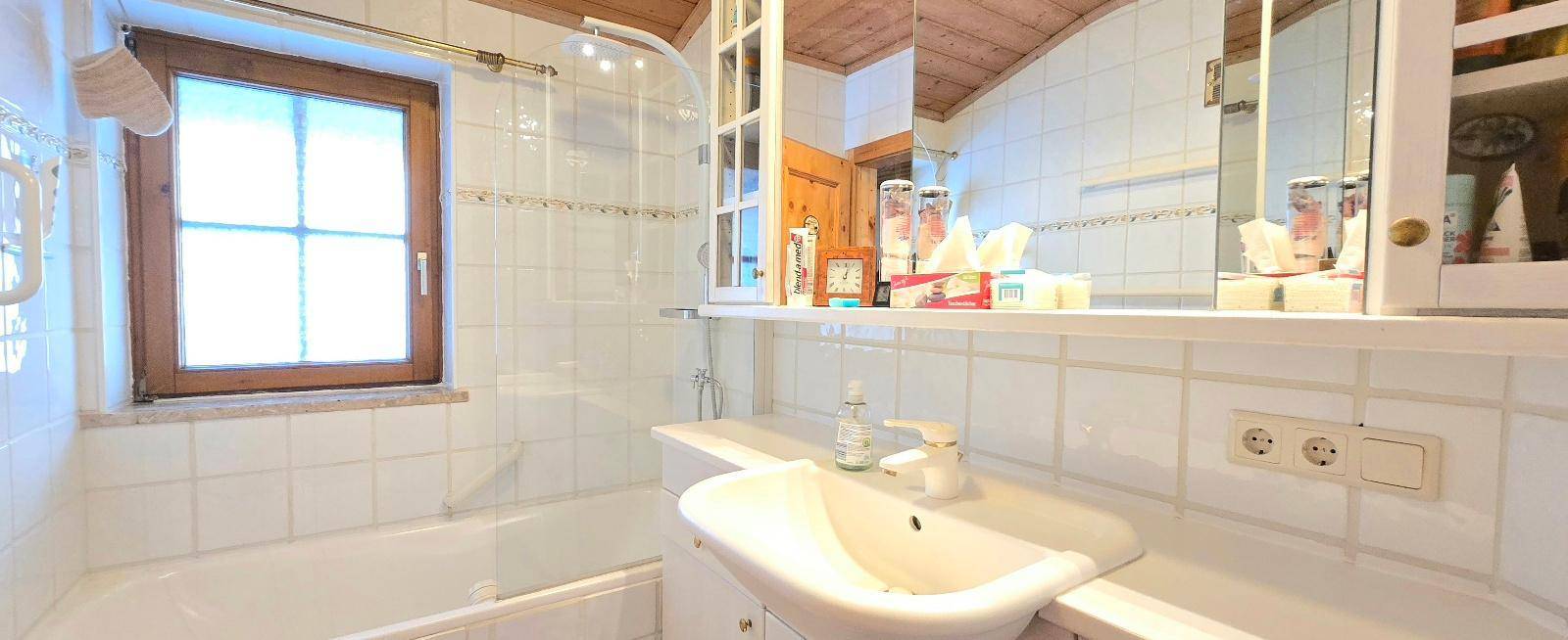 Helles Badezimmer mit Badewanne, Fenster und weißen Fliesen im traditionellen Stil.