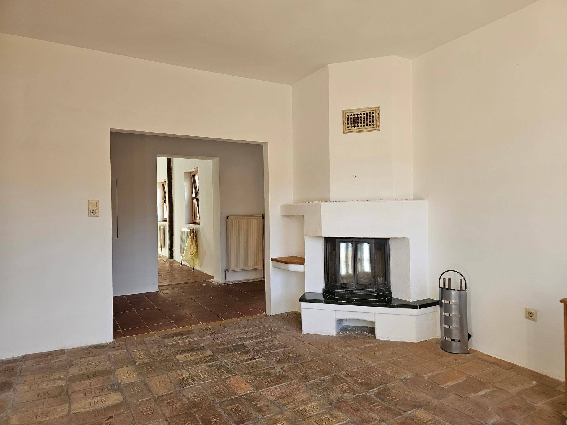 Geräumiges Zimmer mit Eckkamin und traditionellem Terrakotta-Fliesenboden, offen zu einem weiteren Raum.