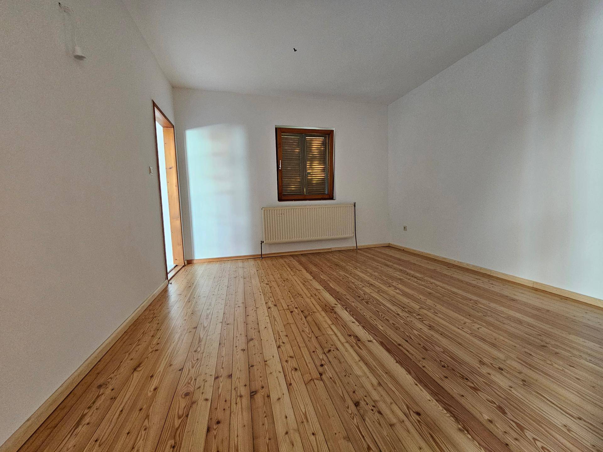 Schlichtes Zimmer mit Holzdielenboden und einem Fenster mit Holzläden, bietet viel Potenzial.