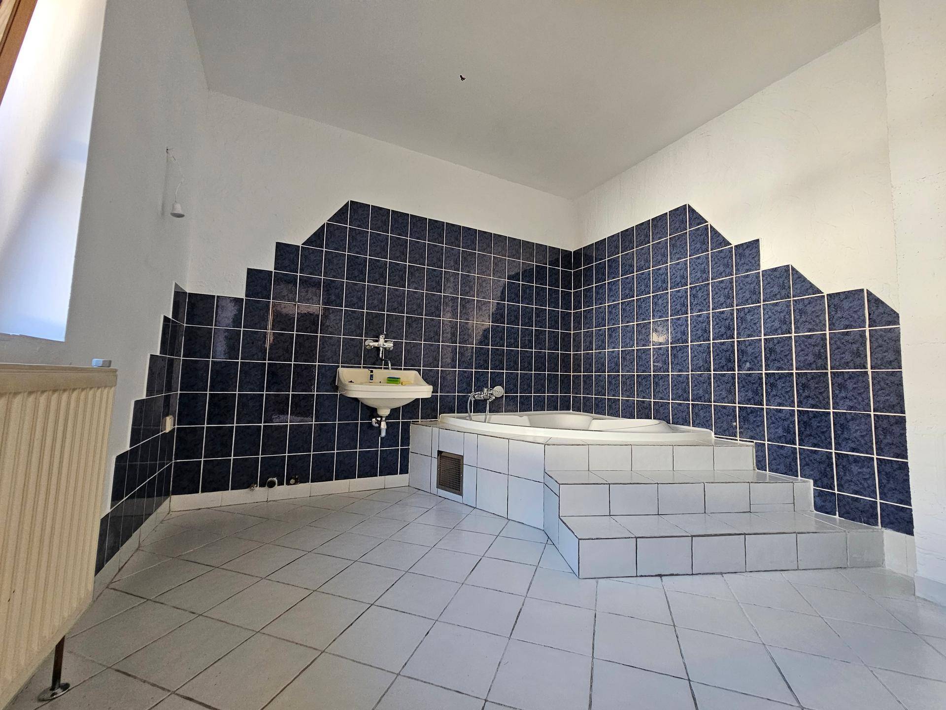 Badezimmer mit blauen und weißen Fliesen, einer eingebauten Eckbadewanne und einem Waschbecken.