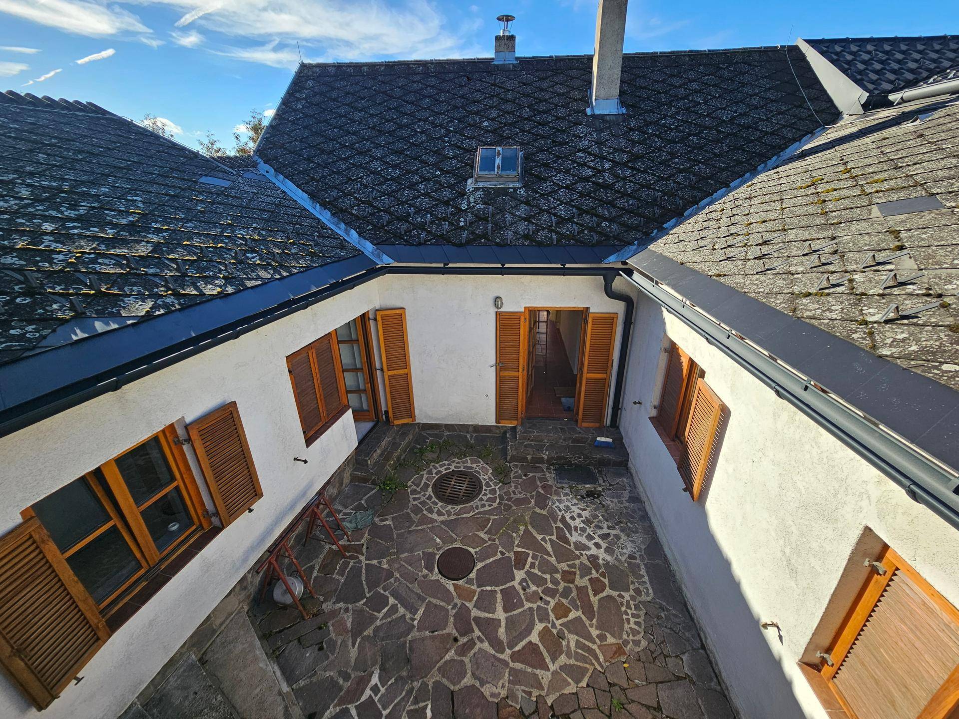 Blick von oben auf einen steinigen Innenhof, umgeben von Dächern und Gebäuden mit Holzläden.