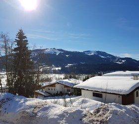 Winterlandschaft mit schneebedeckten Häusern und Bergen unter strahlend blauem Himmel und Sonnenschein.