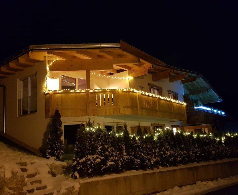 Charmantes Chalet bei Nacht, geschmückt mit Lichterketten und umgeben von verschneiten Bäumen.