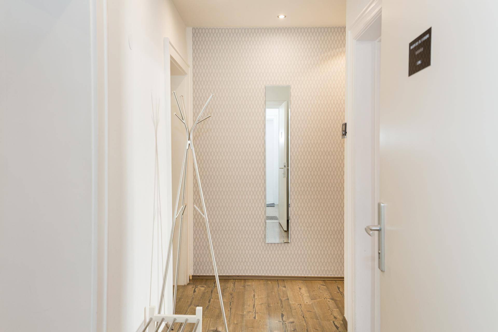 Heller Flur mit gemusterter Tapete, Garderobe und einem schmalen Spiegel an der Wand.