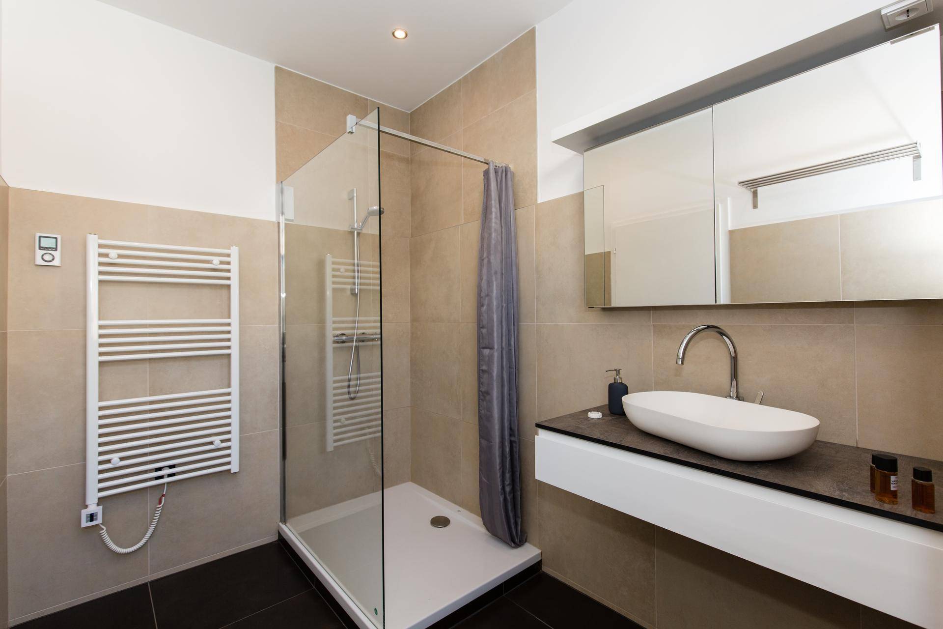 Modernes Badezimmer mit begehbarer Dusche, beheiztem Handtuchhalter und ovalem Waschbecken.